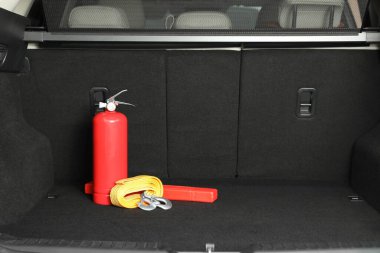 Red fire extinguisher, towing strap and foldable emergency warning triangle in trunk, space for text. Car safety