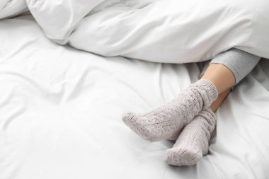 Woman wearing warm socks in comfortable bed, closeup. Space for text