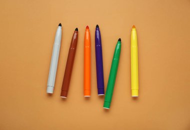 Different colorful markers on light brown background, flat lay