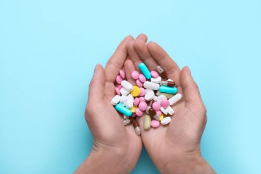 Açık mavi arka planda renkli antidepresanlar tutan kadın.