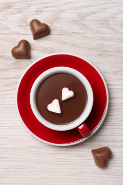 Cup of hot chocolate with heart shaped marshmallows and candies on white wooden table, flat lay