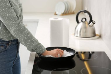 Woman wiping frying pan with paper towel in kitchen, closeup