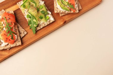 Fresh crunchy crispbreads with cream cheese, cucumber, green onion, salmon and arugula on beige table, top view. Space for text
