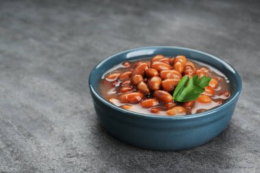 Bowl of canned kidney beans with parsley on grey table, closeup. Space for text