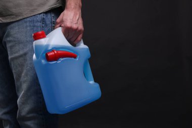 Man holding canister with blue liquid on black background, closeup. Space for text