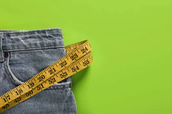 Jeans and measuring tape on green background, top view with space for text. Weight loss concept