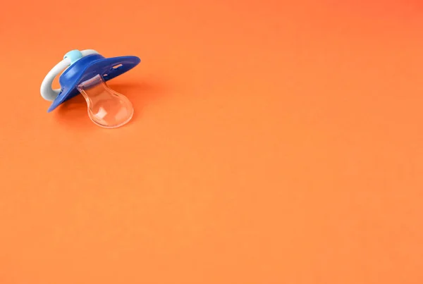 One blue baby pacifier on orange background. Space for text