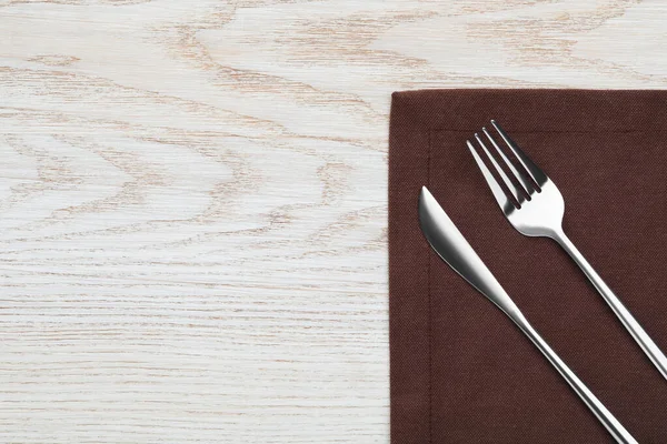 Fork, knife and napkin on white wooden table, top view with space for text. Stylish shiny cutlery set