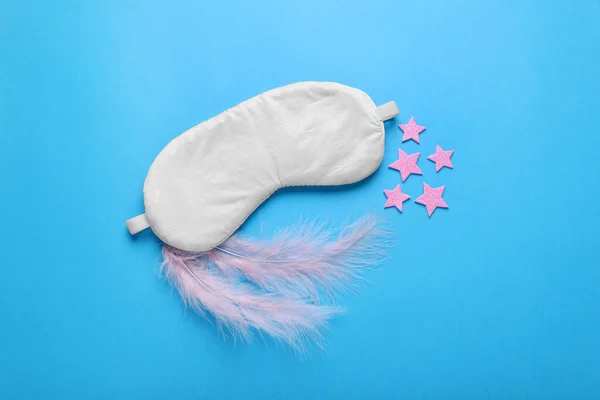 Soft sleep mask, decorative stars and pink feathers on light blue background, flat lay