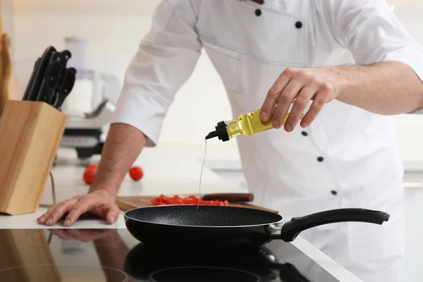 Chef pouring oil from bottle into frying pan indoors, closeup