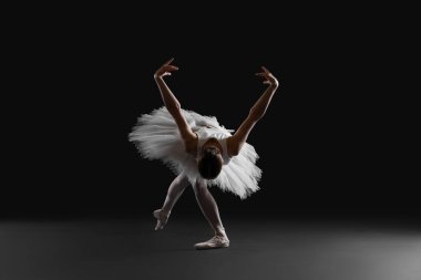Young ballerina practicing dance moves on black background