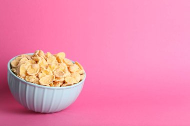 Bowl of tasty crispy corn flakes on pink background, space for text