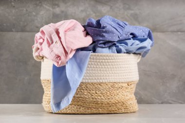 Çamaşır sepeti ve gri duvarın yanında giysiler.