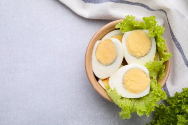 Fresh hard boiled eggs and lettuce on light grey table, top view. Space for text