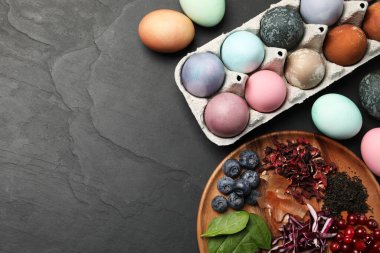 Naturally painted Easter eggs on black table, flat lay. Red cabbage, spinach, hibiscus, tea, onion, cranberries and blueberries used for coloring