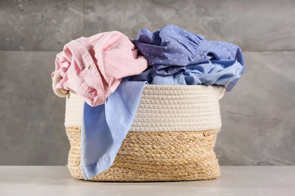 Çamaşır sepeti ve gri duvarın yanında giysiler.