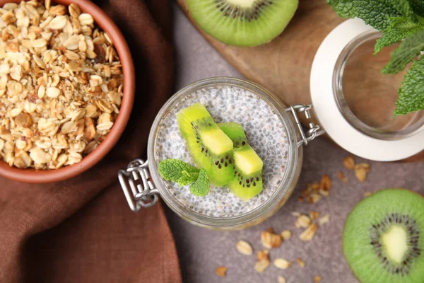 Delicious dessert with kiwi, fresh cut fruits and muesli on brown table, flat lay