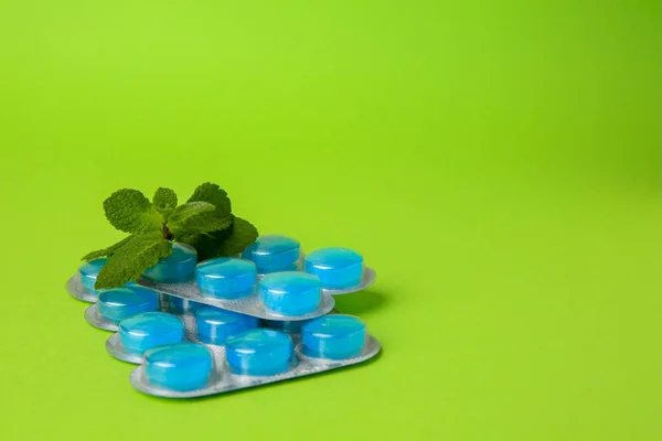 Blisters with cough drops and mint leaves on light green background. Space for text