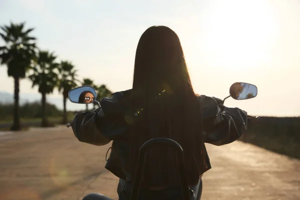 Woman riding motorcycle at sunset, back view