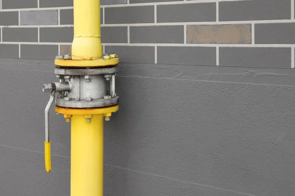 Yellow gas pipe with valve near brown wall outdoors, space for text