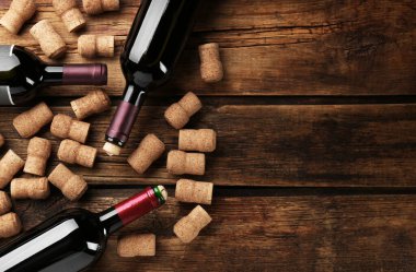 Bottles with wine, corkscrew and corks on wooden table, flat lay. Space for text