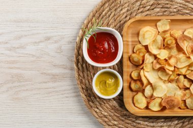Tasty homemade parsnip chips with different sauces on white wooden table, flat lay. Space for text