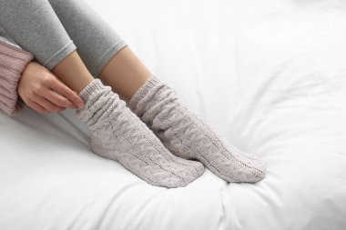 Woman wearing warm socks in comfortable bed, closeup. Space for text