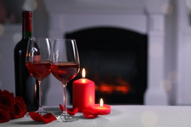 Glasses of red wine, burning candles and rose flowers on grey table indoors, space for text. Romantic atmosphere