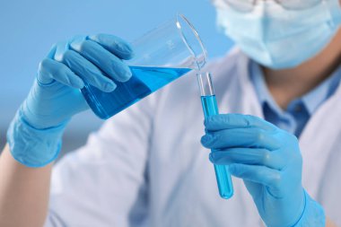 Scientist working with beaker and test tube on light blue background, closeup