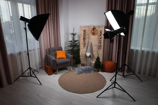 Beautiful Christmas themed photo zone with professional equipment, trees and armchair in room