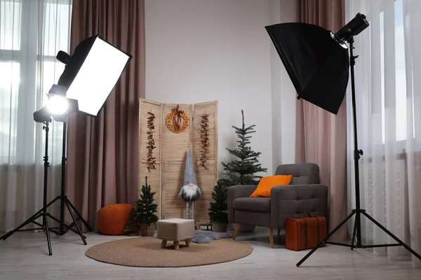 Beautiful Christmas themed photo zone with professional equipment, trees and armchair in room