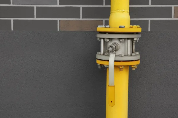 Yellow gas pipe with valve near brown wall outdoors, space for text