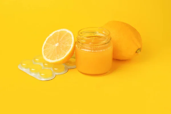 Cough drops, fresh lemons and honey on yellow background