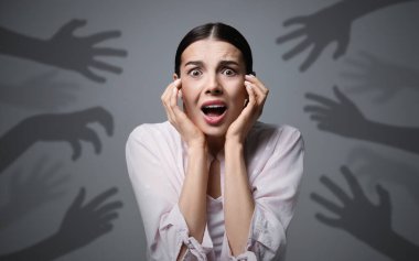 Paranoid delusion. Scared woman screaming on grey background. Shadows of hands reaching for her symbolizing fear and anxiety clipart