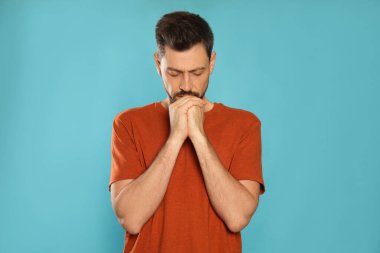 Elleri sıkıca bağlı bir adam turkuaz arka planda dua ediyor.