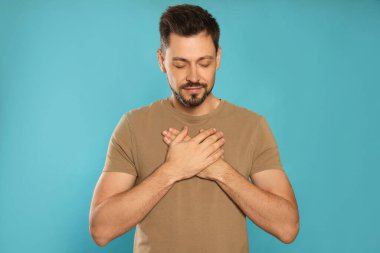 Elleri sıkıca bağlı bir adam turkuaz arka planda dua ediyor.