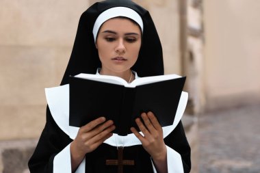 Young nun reading Bible near building outdoors