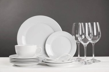 Set of clean dishware and glasses on white wooden table against grey background