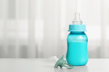Feeding bottle with milk and pacifier on white table indoors, space for text