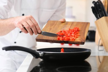 Chef putting cut tomatoes into frying pan indoors, closeup