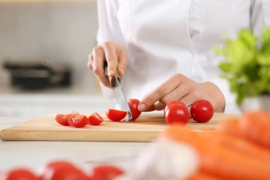 Professional chef cutting fresh tomatoes at white marble table in kitchen, closeup