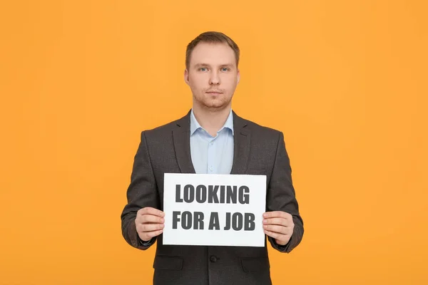 Unemployed man holding sign with phrase Looking For A Job on orange background