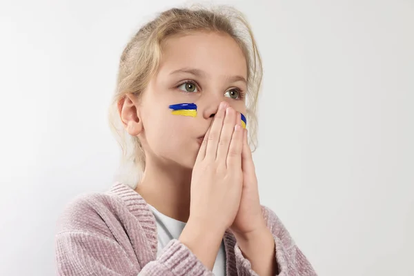 Little girl with drawings of Ukrainian flag on face and clasped hands against white background