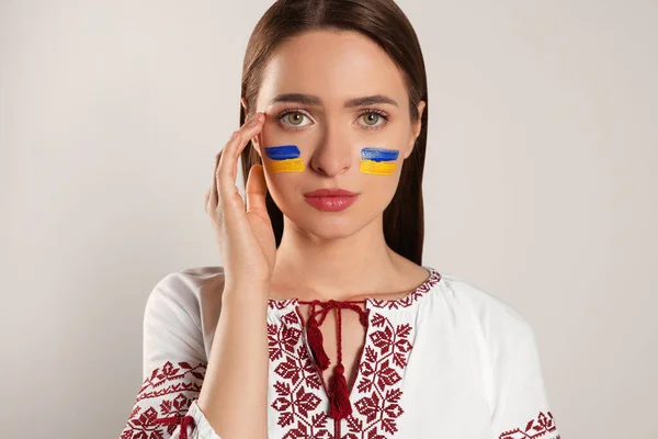 Young woman with drawings of Ukrainian flag on face against beige background