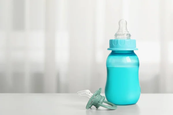Feeding bottle with milk and pacifier on white table indoors, space for text