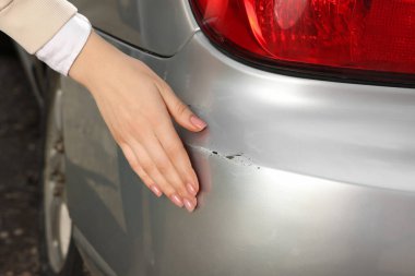 Woman near car with scratch outdoors, closeup view
