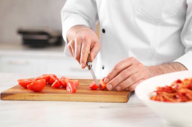 Chef cutting tomatoes at marble table in kitchen, closeup