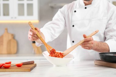 Professional chef putting delicious spaghetti into bowl at marble table in kitchen, closeup