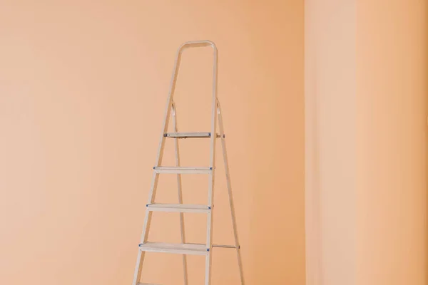 Ladder near pale orange wall. Room renovation