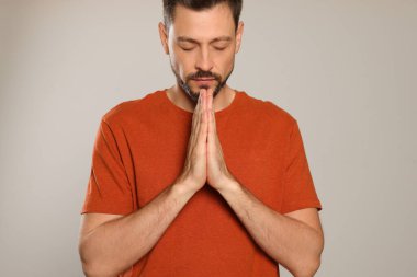 Elleri sıkıca bağlı açık gri arka planda dua eden adam.
